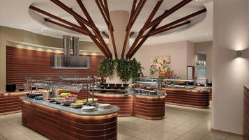 A modern kitchen with a central island, multiple food stations, and a large plant.