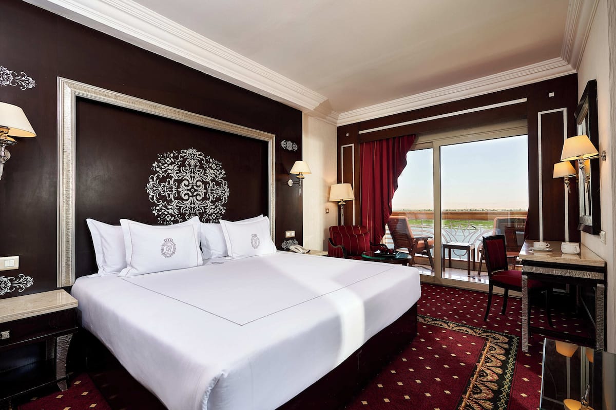 Quarto de hotel com uma cama grande, uma escrivaninha, uma cadeira e vista para o exterior.
