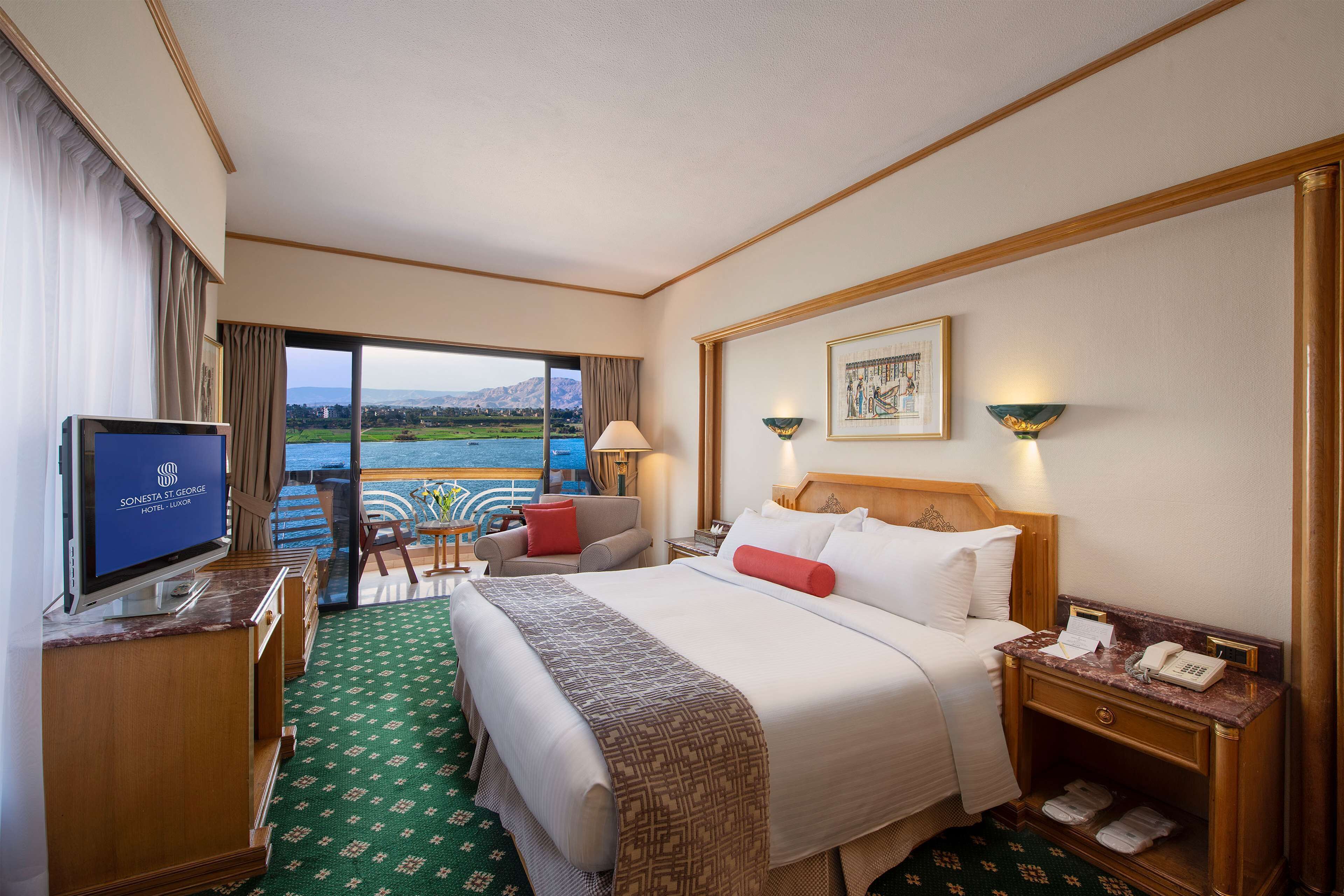 A hotel room with a large bed, a TV, a desk, and a view of a body of water.