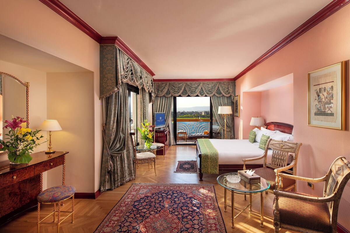 Quarto de hotel com cama, escrivaninha, cadeira, mesa e vista para o exterior.