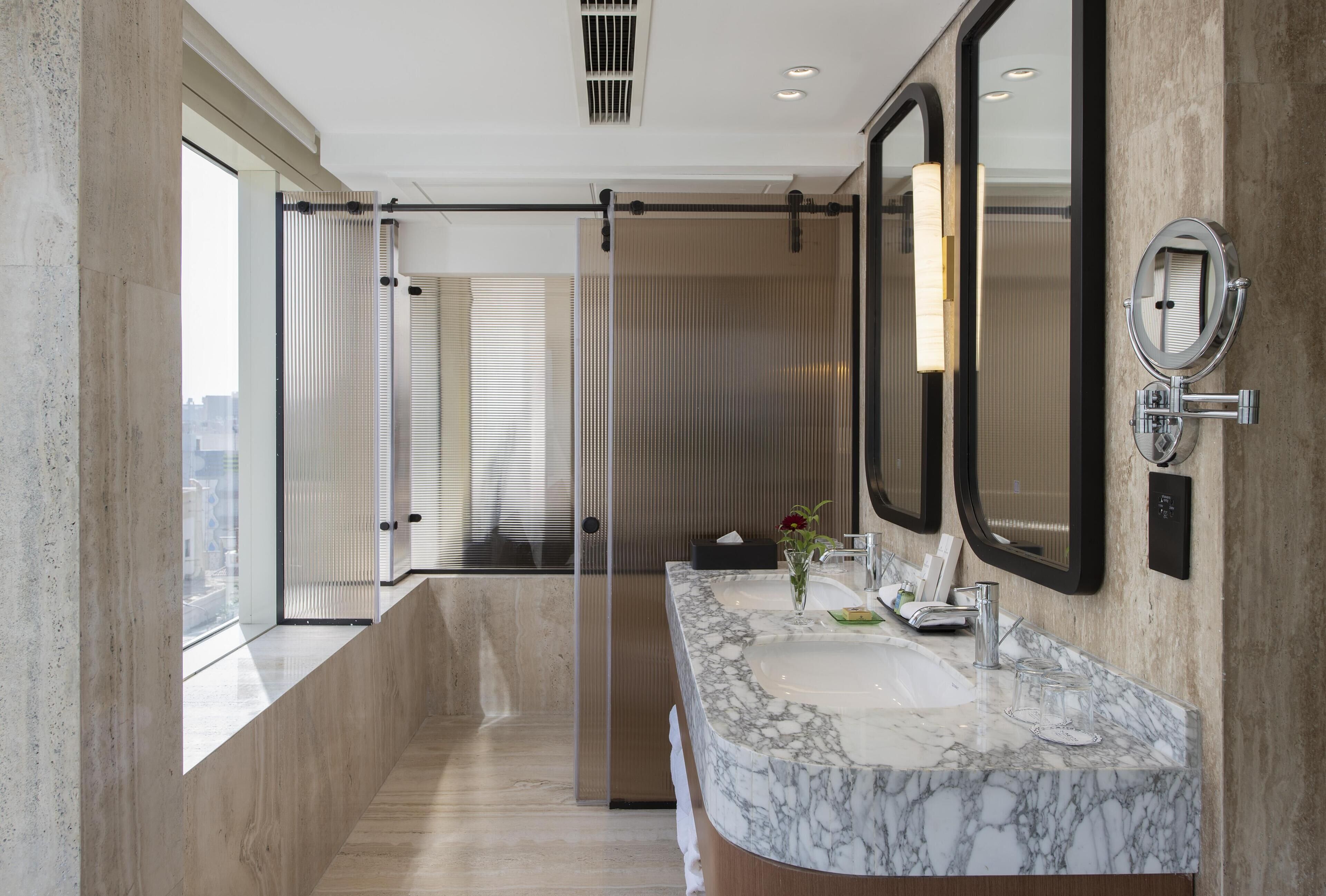 Un baño moderno con lavamanos de mármol, espejos amplios y vistas a través de una puerta corredera.