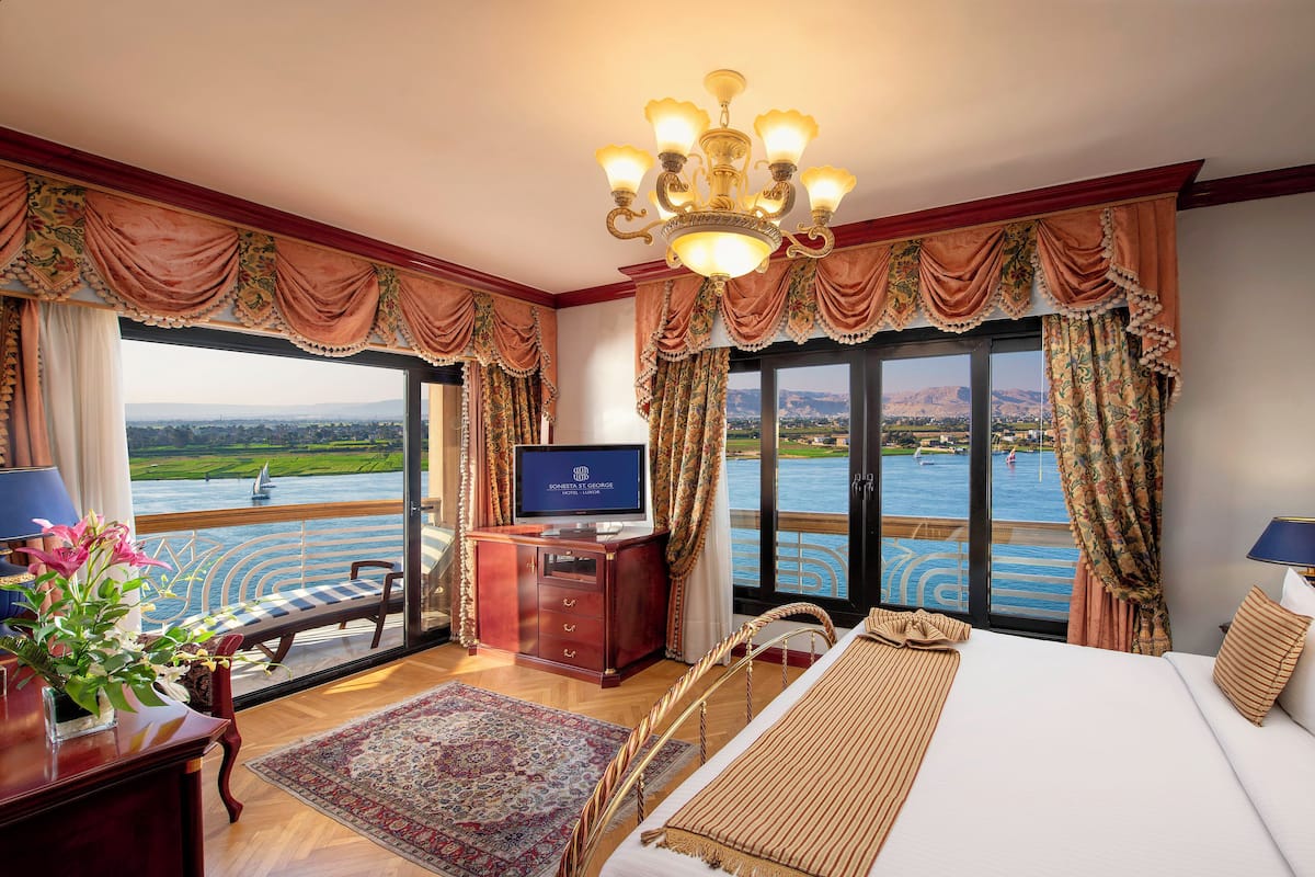 Quarto de hotel com uma cama grande, uma escrivaninha com computador, televisão e vista para a água.