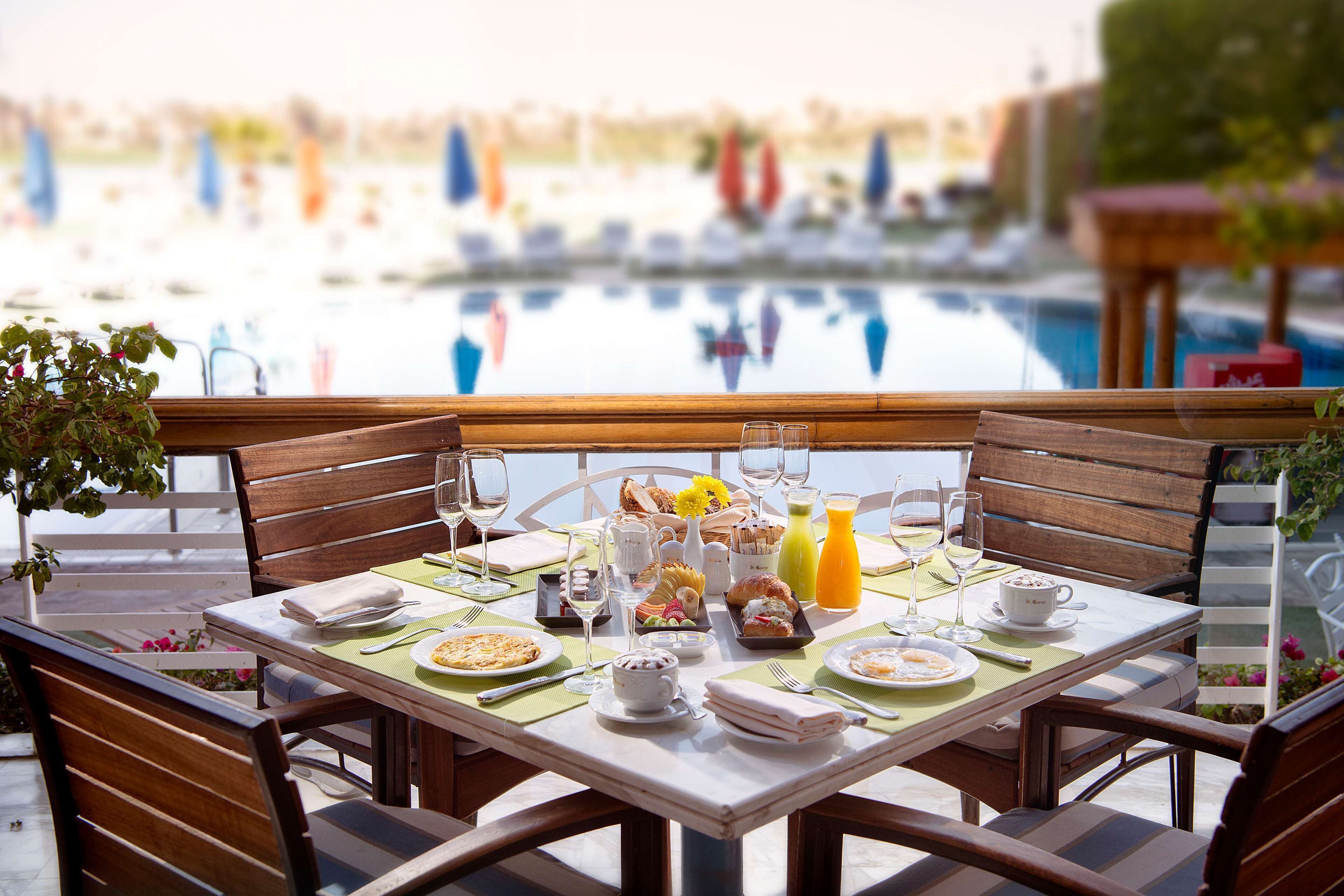 Mesa de desayuno dispuesta con platos, vasos y vista a un área de piscina.