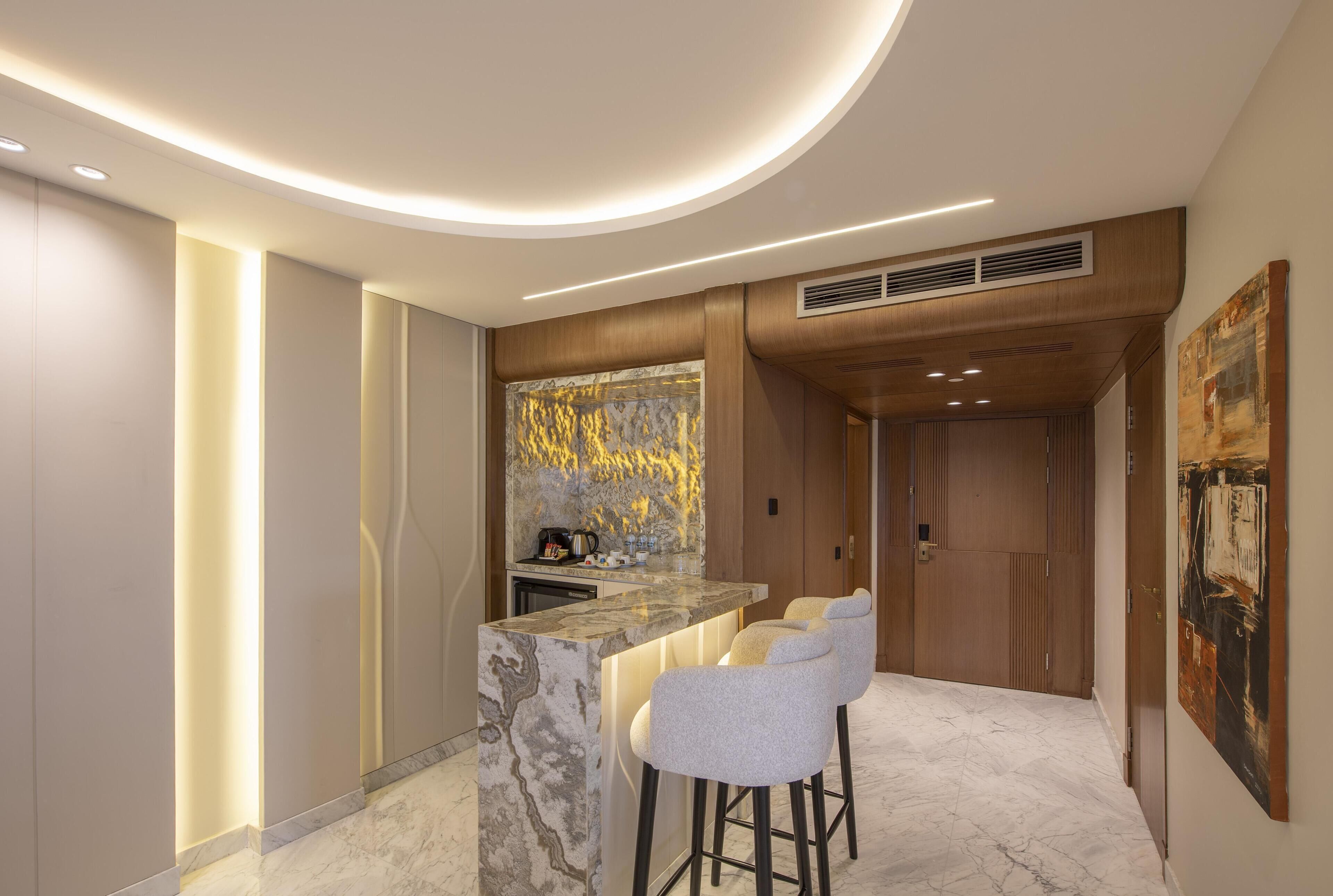 A modern kitchen with a marble countertop, bar stools, and a built-in coffee machine.