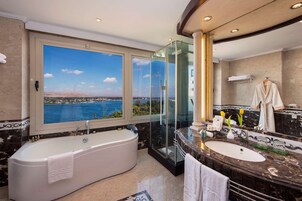 A luxurious bathroom with a large bathtub, a vanity with a mirror, and a view of a body of water.