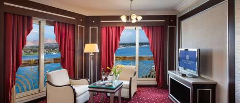 A hotel room with a large window, a television, a table with a vase of flowers, and a red carpet.