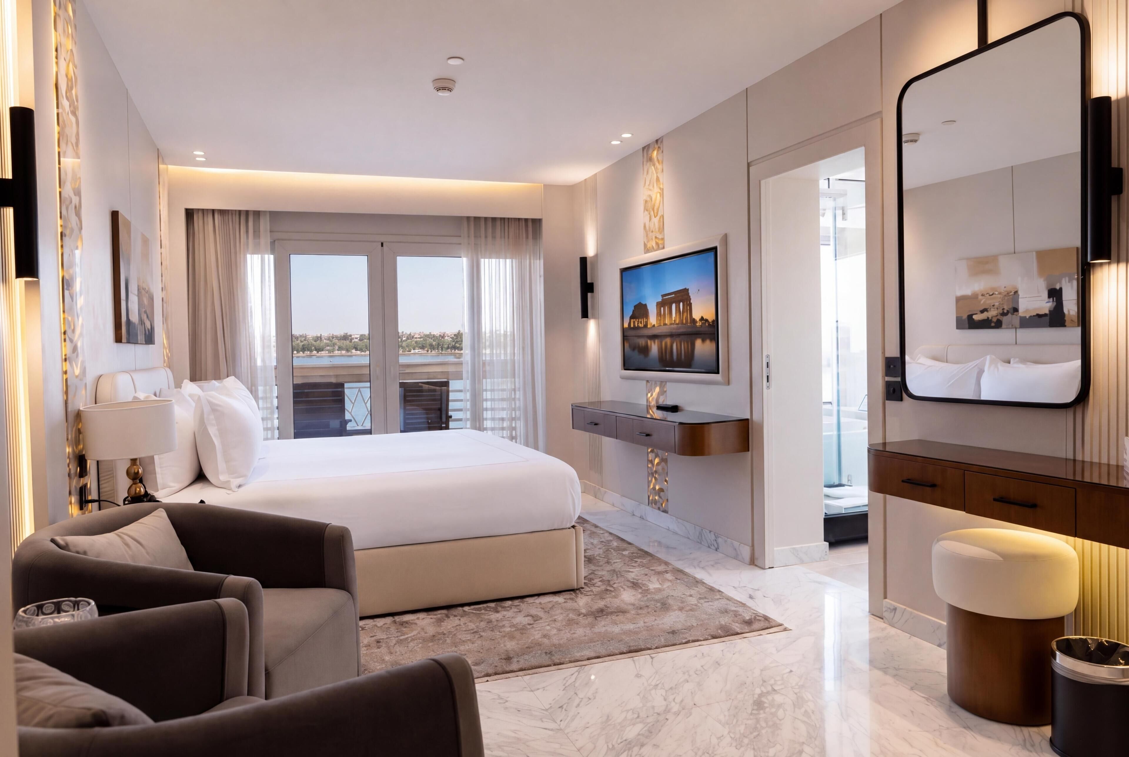 A modern hotel room with a large bed, a TV, a desk, and a bathroom.