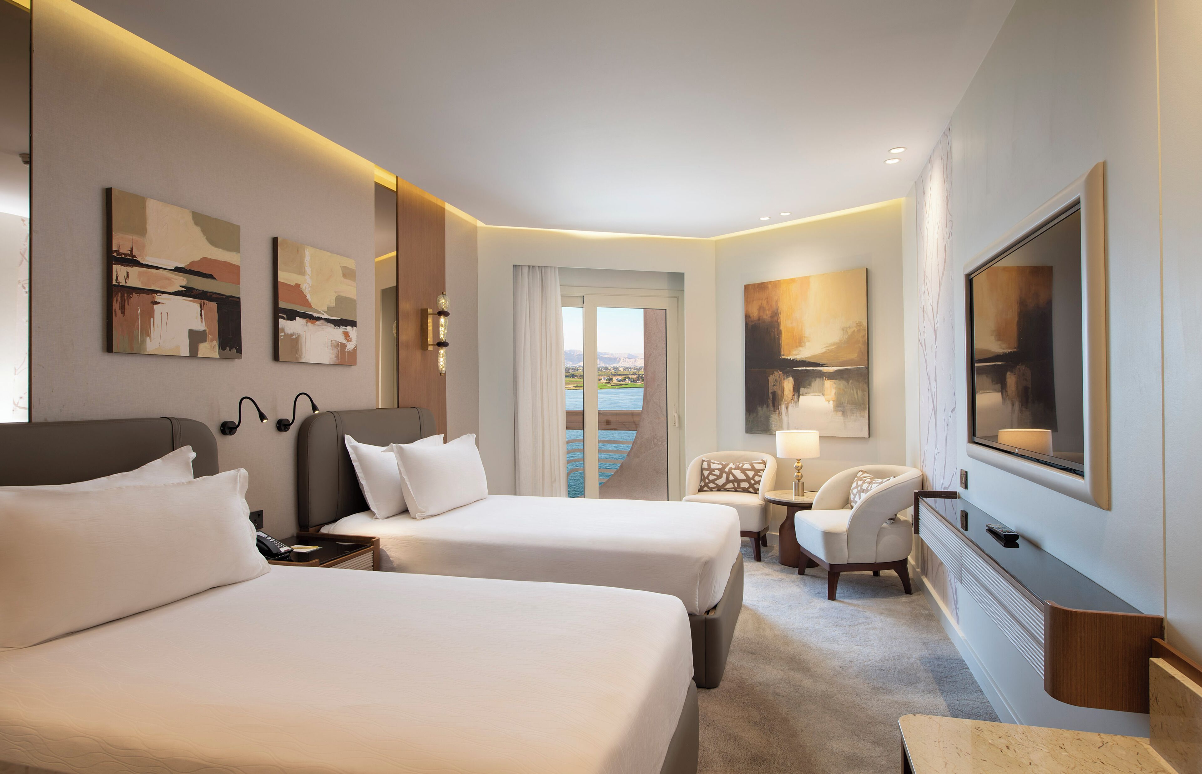 Una habitación de hotel con dos camas, televisión, obras de arte en las paredes y vistas al exterior.