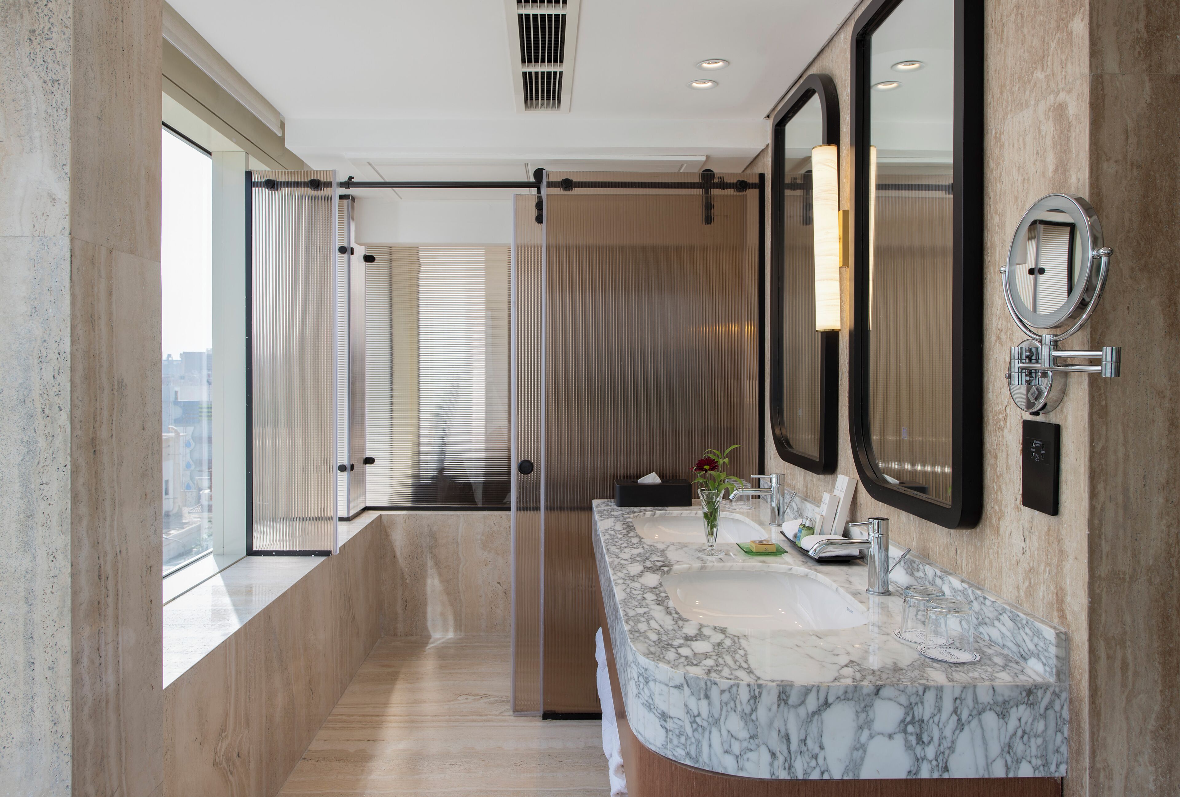 A modern bathroom with a large mirror, marble countertop, and a view through a glass door.