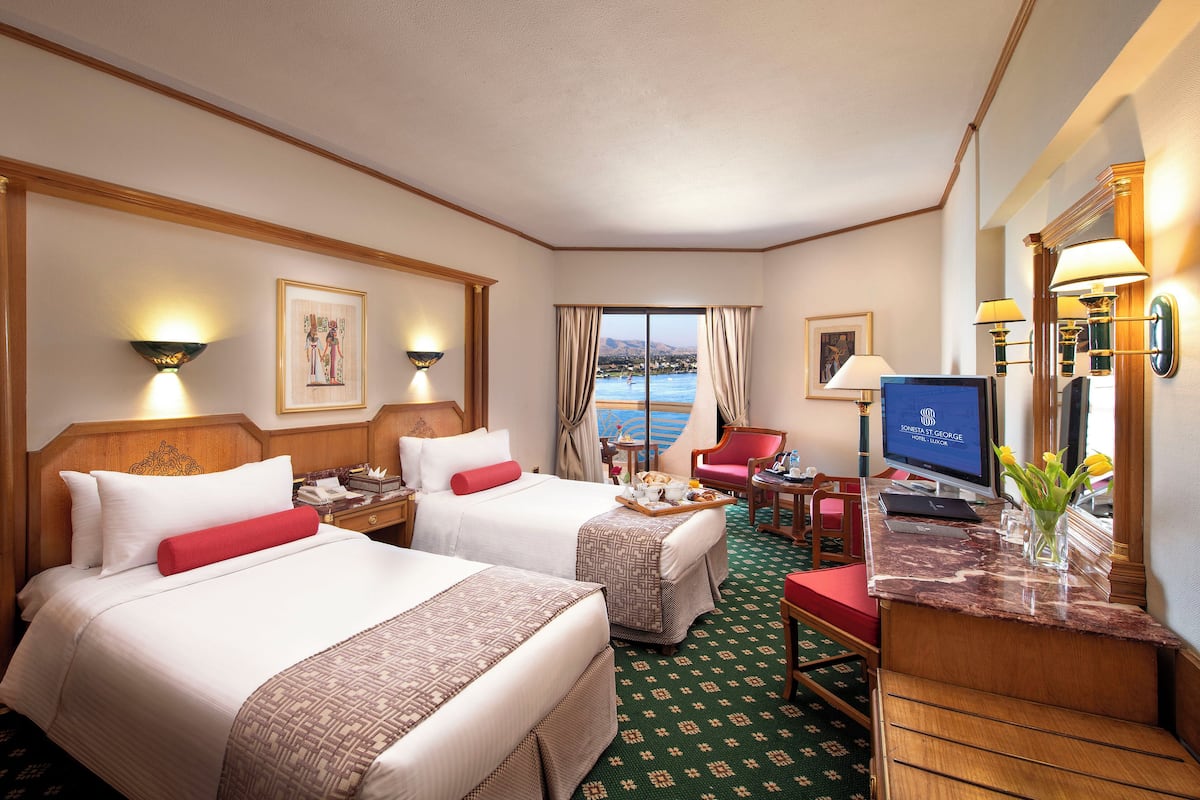 Quarto de hotel com duas camas, uma escrivaninha, televisão e vista para o mar.