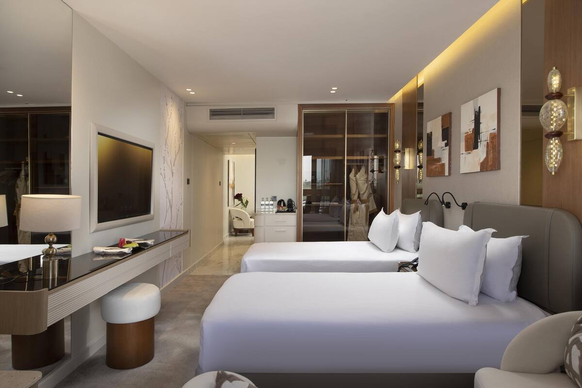 Quarto de hotel moderno com duas camas, uma escrivaninha e um espelho.