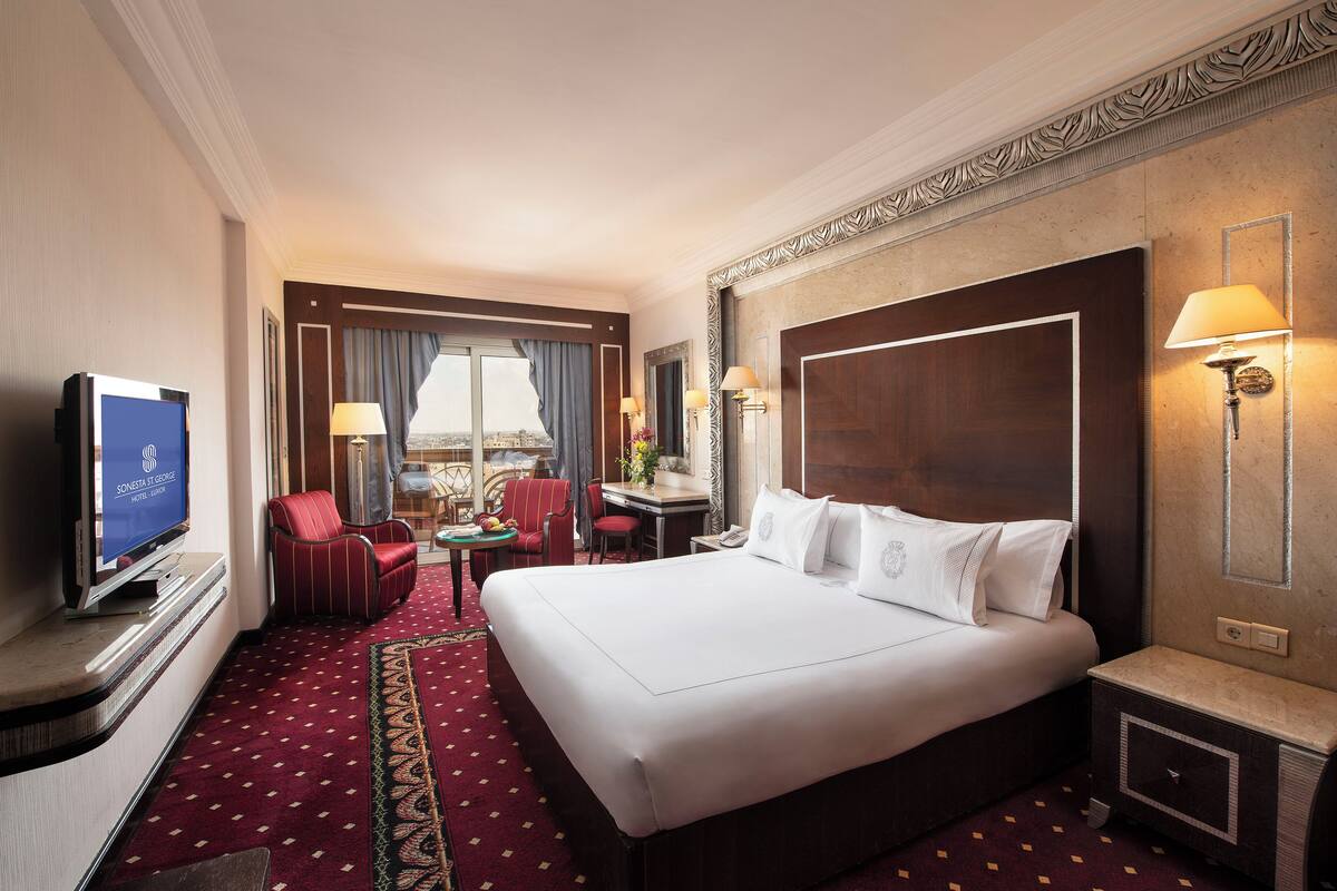 Quarto de hotel com uma cama grande, uma escrivaninha com cadeira, televisão e vista para a cidade.