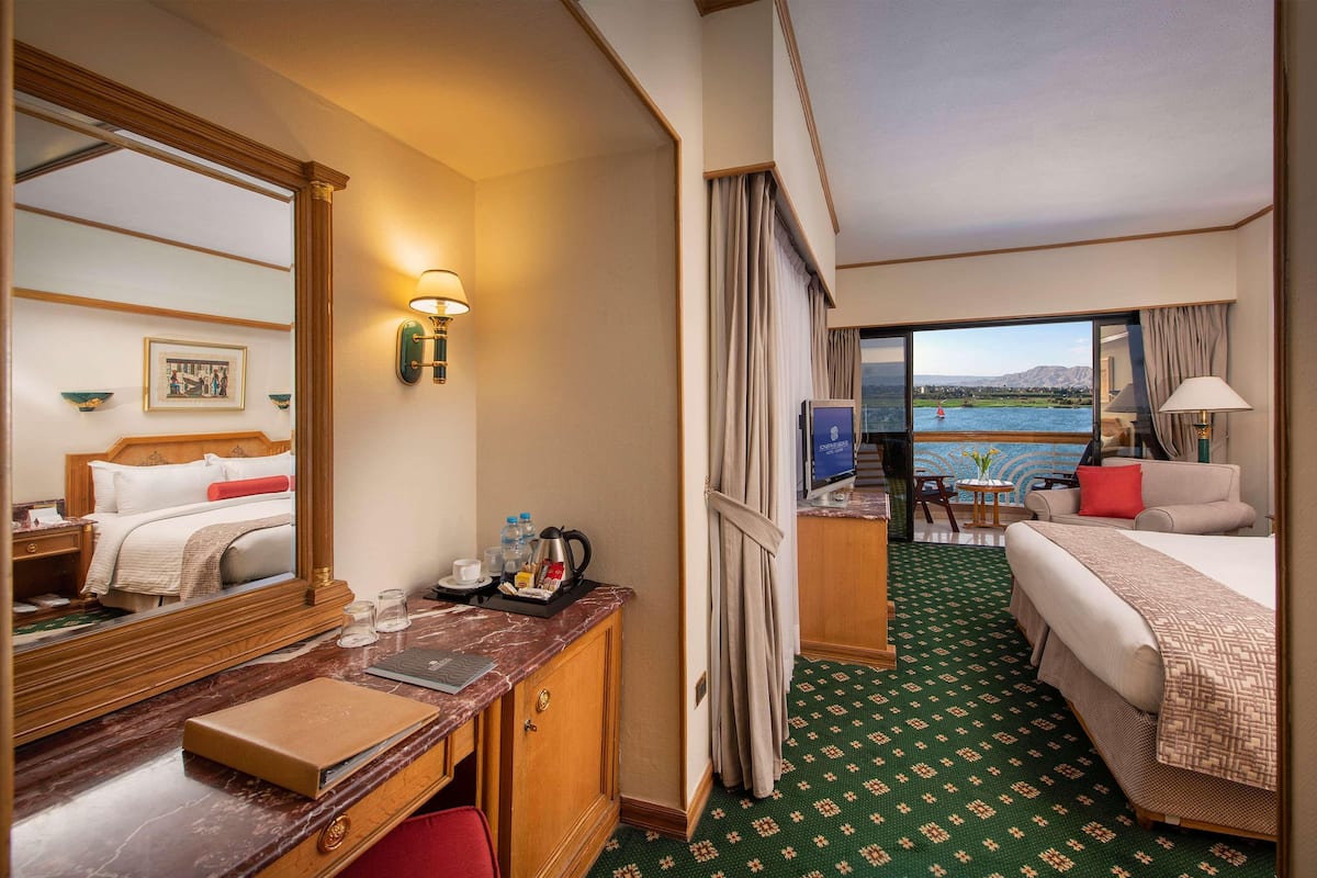 A hotel room with a bed, a desk, a chair, a television, and a view of the water.