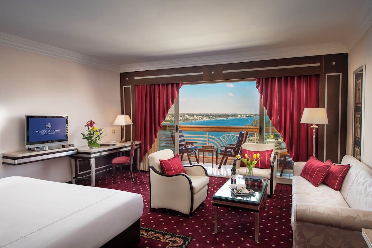Quarto de hotel com cama, escrivaninha com computador, sofá, poltrona, mesa de centro e vista para o mar.