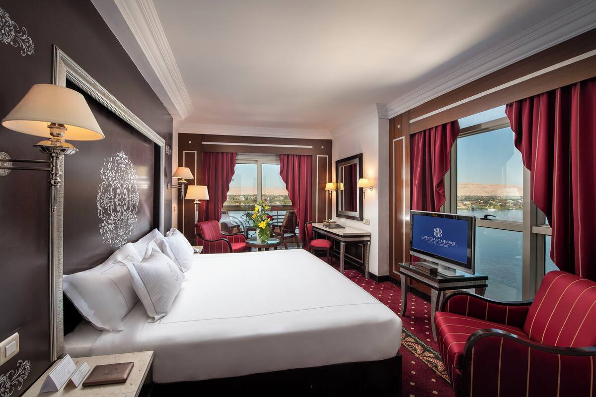 Quarto de hotel com uma cama grande, uma escrivaninha, uma televisão e vista para a água.