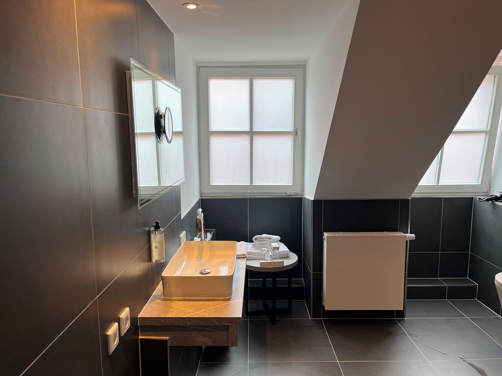 Une salle de bain moderne avec un grand miroir, un meuble-lavabo en bois, un évier et un porte-serviettes.