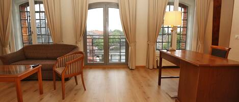 Un salón amplio con sofá, sillas, una mesa de madera y un balcón con cortinas.