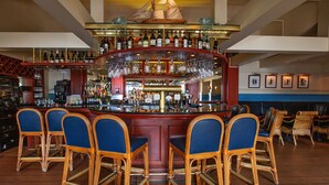 A bar area with a central bar counter, multiple seating options including bar stools and chairs, and a variety of bottles and glasses on shelves. - DORMERO Hotel Bergström Lüneburg (Lueneburg)