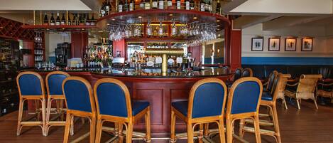 Zona de bar con barra central, diversas opciones de asientos que incluyen taburetes y sillas, y una variedad de botellas y vasos en estanterías.