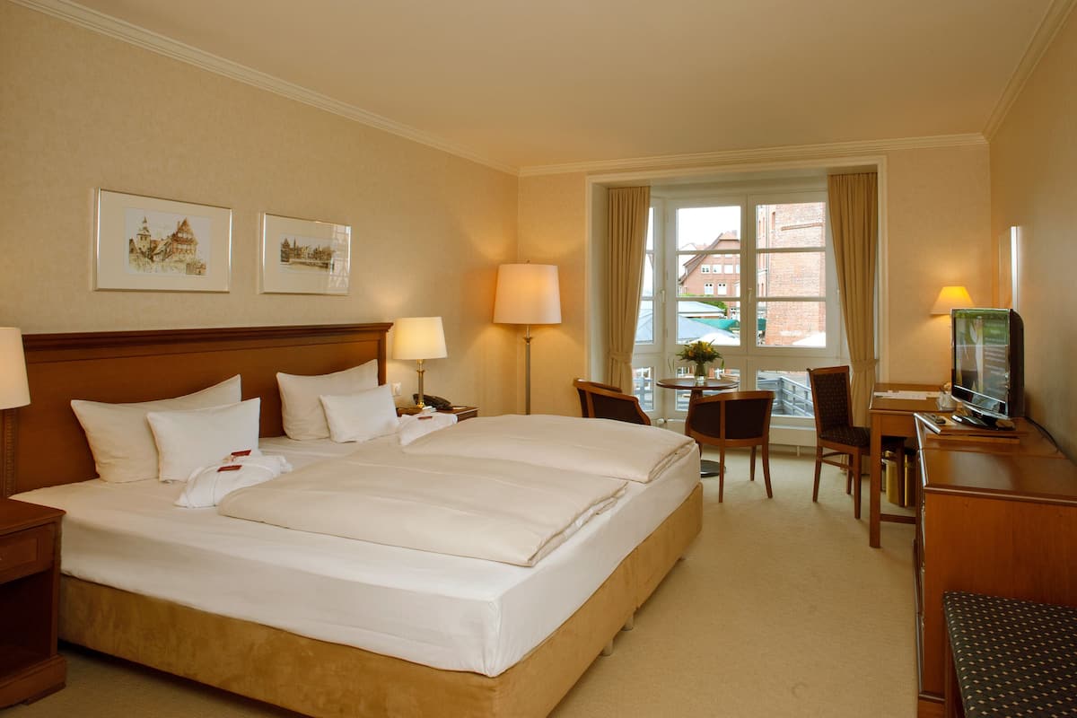 Une chambre d’hôtel avec un grand lit, deux tables de chevet avec des lampes, un bureau avec une chaise, une télévision et des tableaux encadrés au mur.