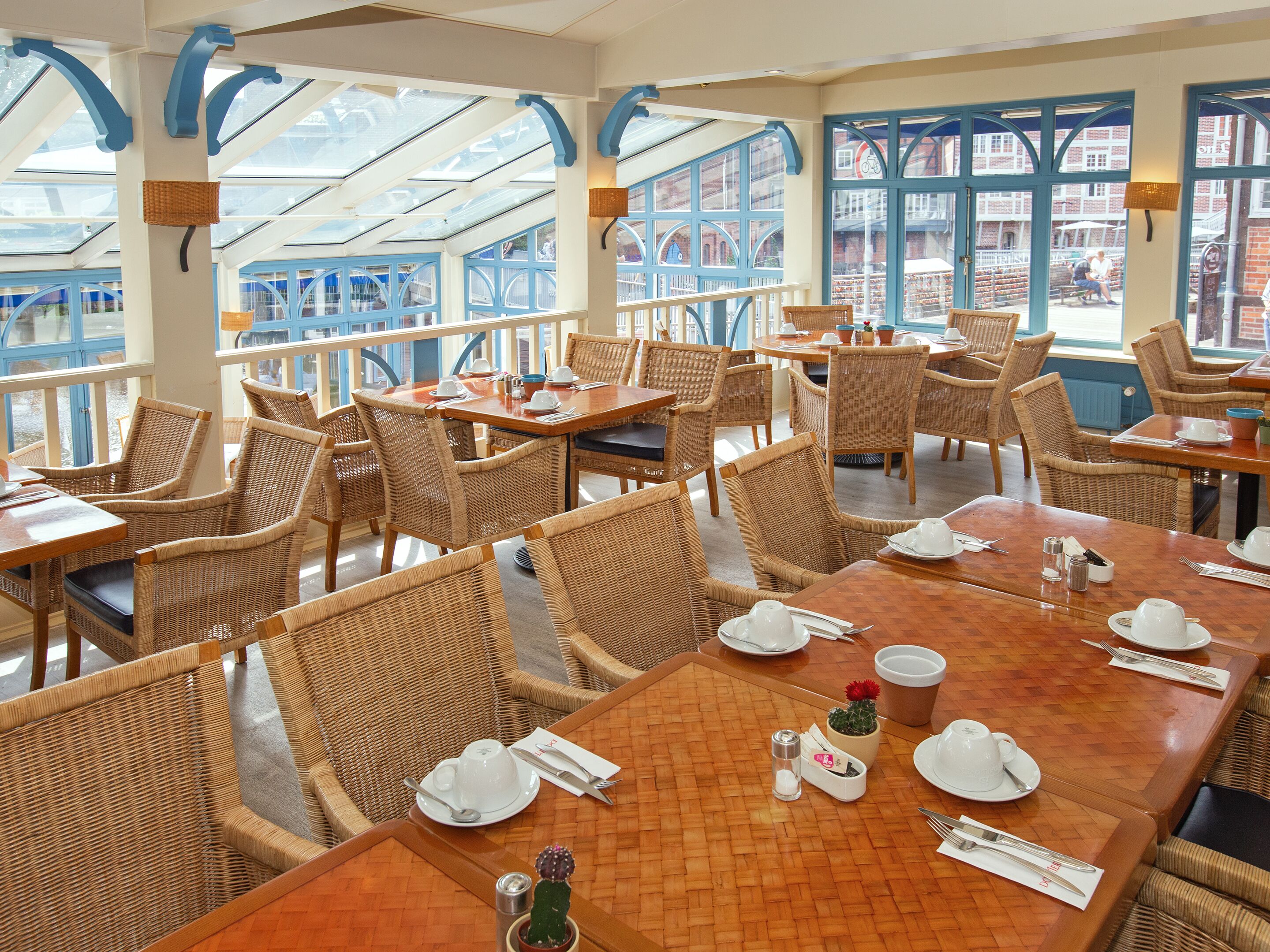 Un restaurant doté de mobilier en osier, de grandes fenêtres et offrant une vue sur la rue.