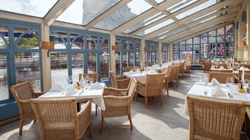 A restaurant with outdoor seating, large windows, and wicker chairs.