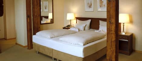 A double bed with white linens, two bedside tables with lamps, and framed artwork on the wall.