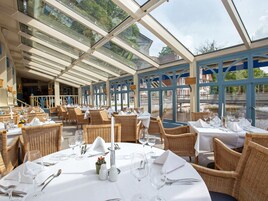Un restaurante con terraza, techo de cristal, sillas de mimbre y mesas preparadas para comer.