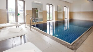 A swimming pool with a glass wall, a changing room with towels, and a view of a building outside. - DORMERO Hotel Bergström Lüneburg (Lueneburg)
