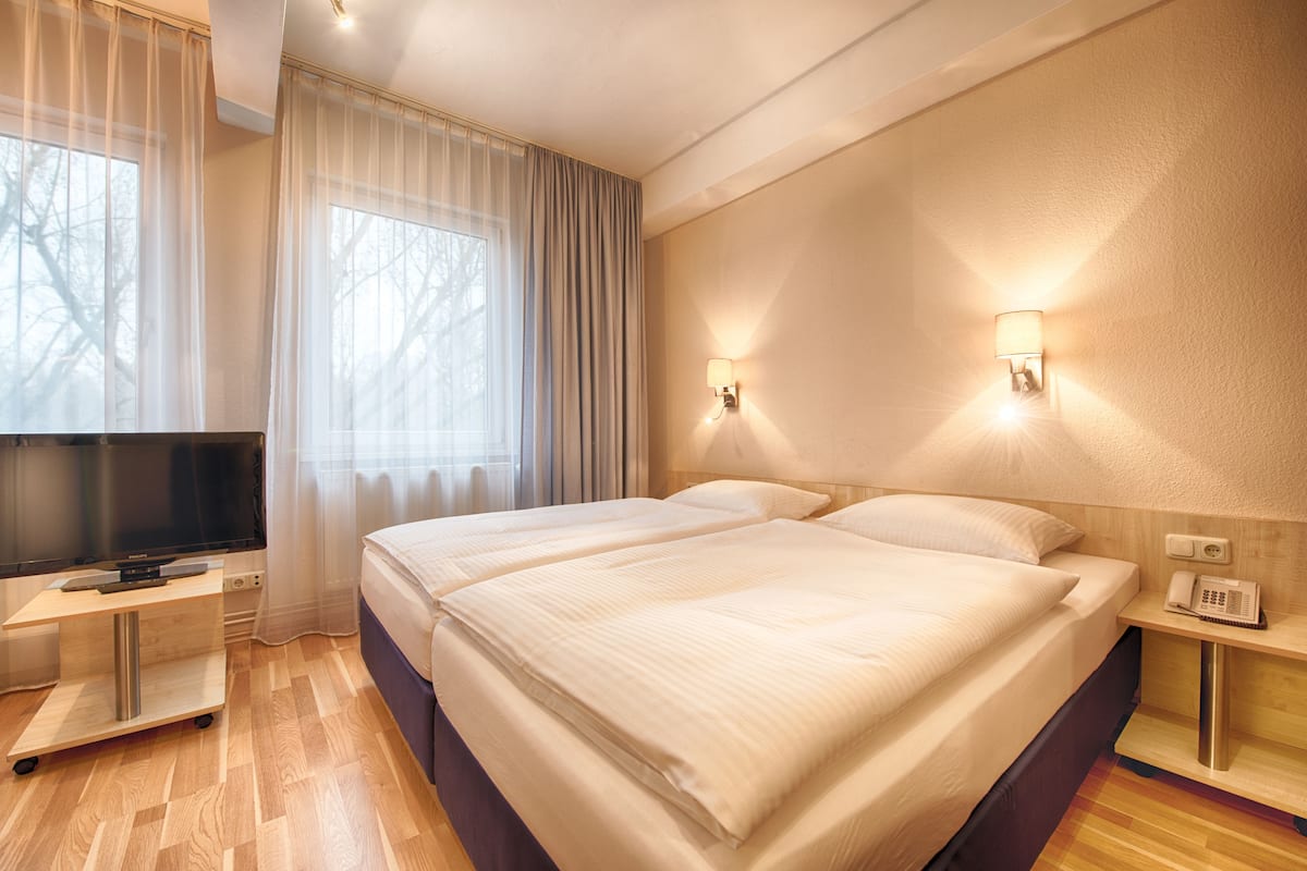 A hotel room with a large bed, a TV, a bedside table, and a lamp.