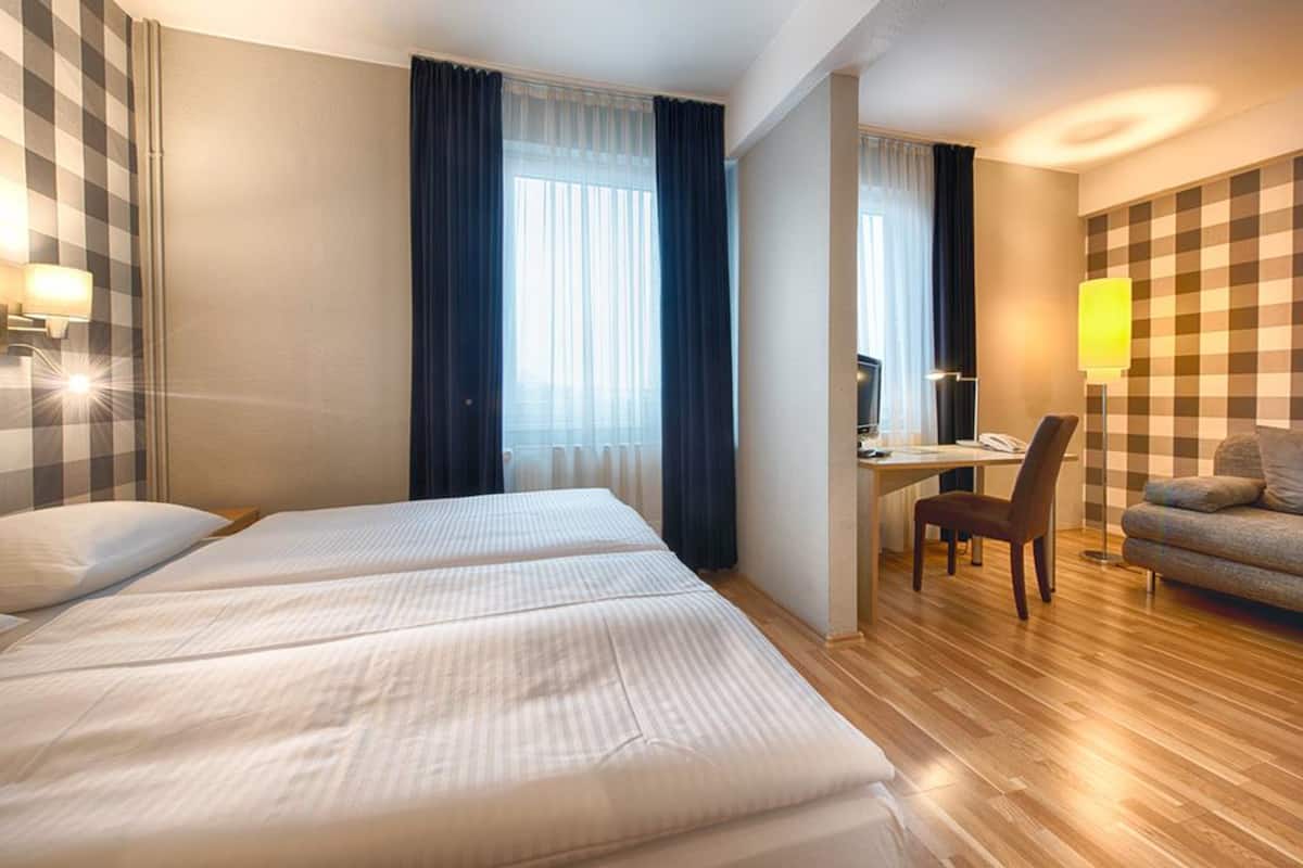 A hotel room with two beds, a desk, a chair, and a sofa.