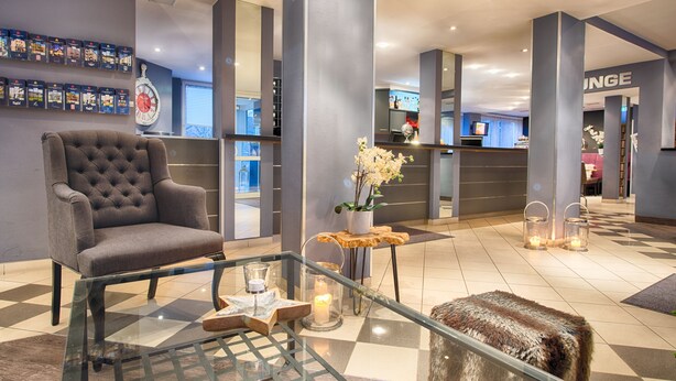 A lobby with a tufted armchair, a glass coffee table with candles, and a fur ottoman. - Enjoy Hotel Berlin City Messe (Berlin)