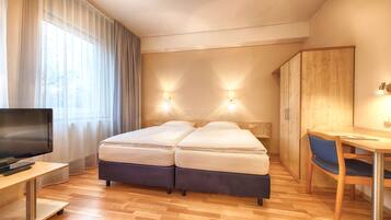 A hotel room with two beds, a desk, a chair, a TV, and a wardrobe.