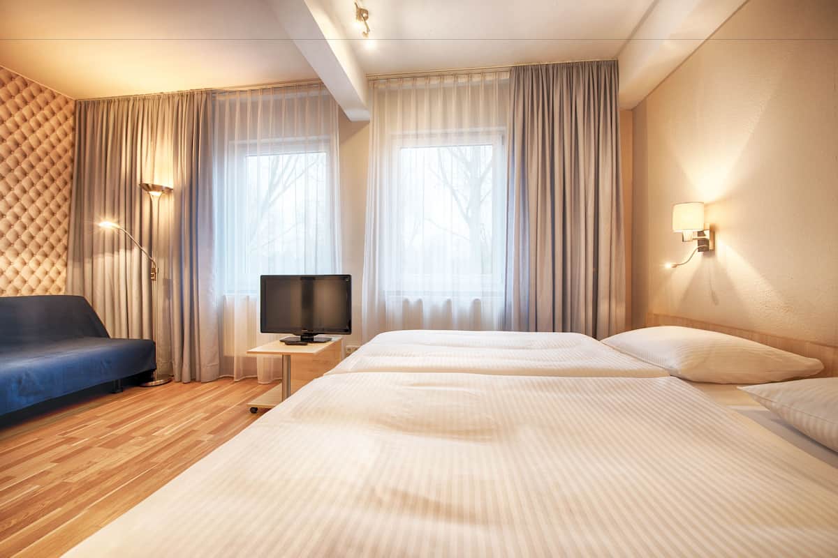 A hotel room with a large bed, a TV on a small table, a blue sofa, and curtains on the windows.