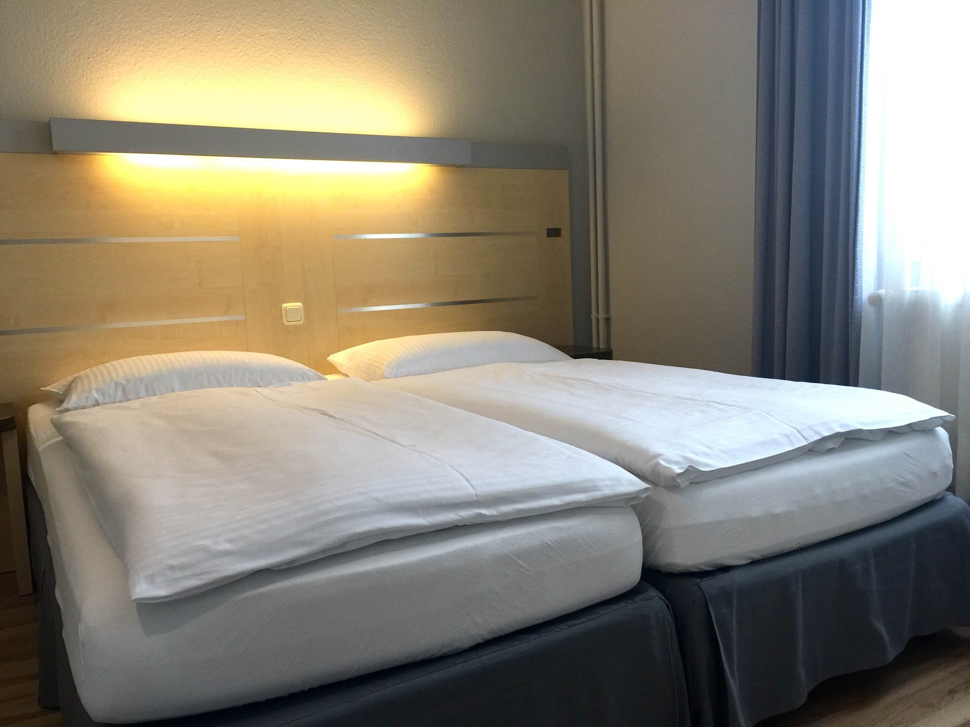 Una cama doble con ropa de cama blanca en una habitación de hotel.