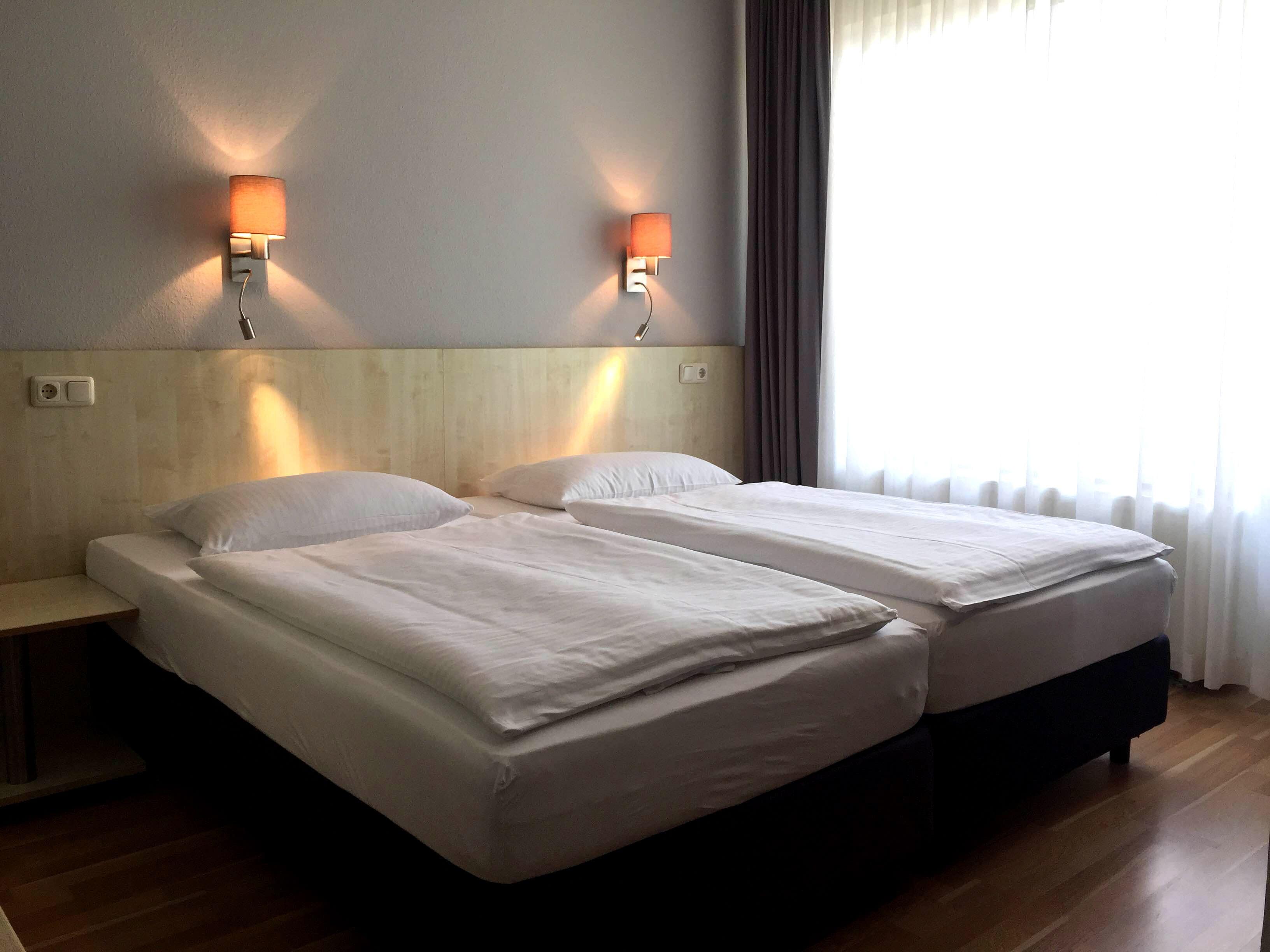 Une chambre d’hôtel avec deux lits, une tête de lit en bois, des tables de chevet et des lampes fixées au mur.