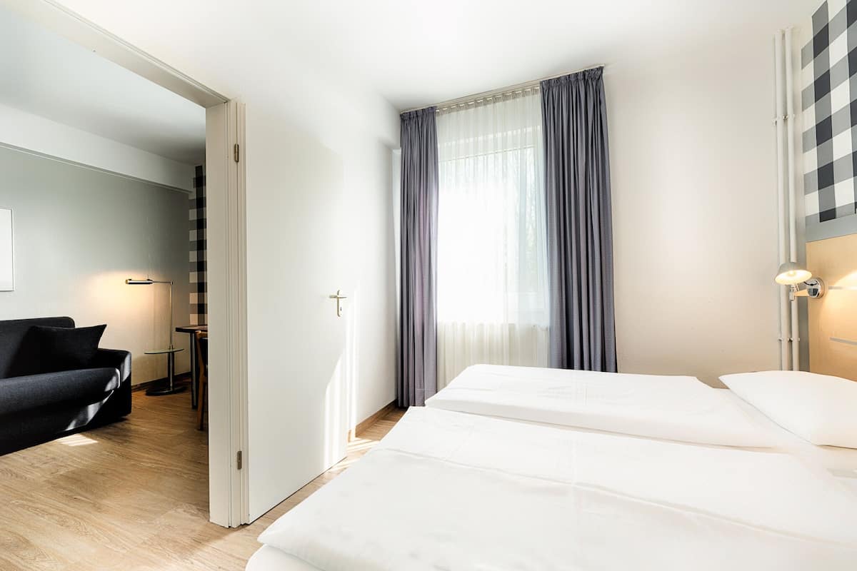 A hotel room with a bed, a chair, a desk, and a window with curtains.