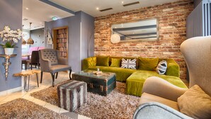 A cozy living room with a green sofa, a leather armchair, and a vintage trunk as a coffee table. - Enjoy Hotel Berlin City Messe (Berlin)
