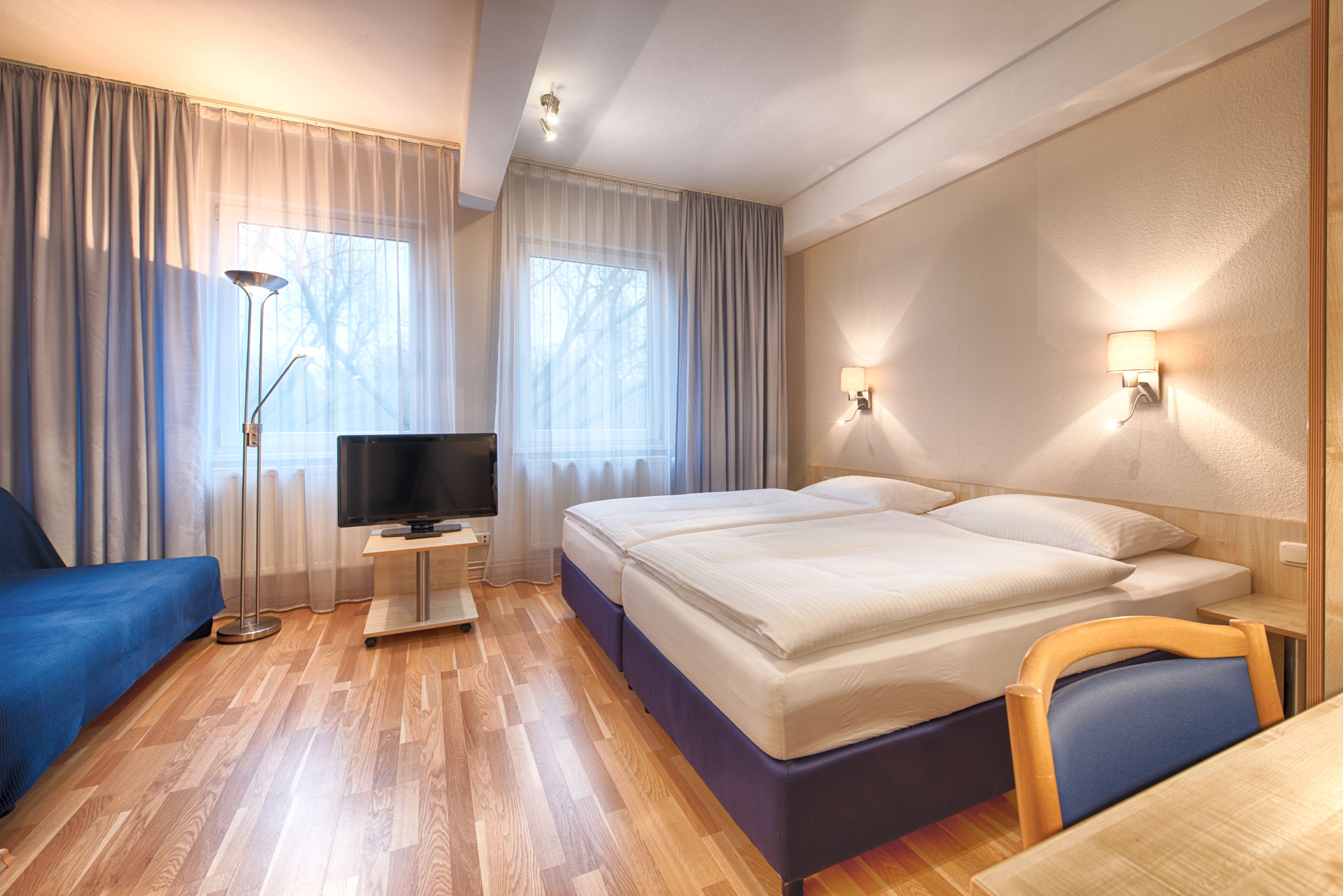 A hotel room with a bed, a TV, a desk, and a chair.