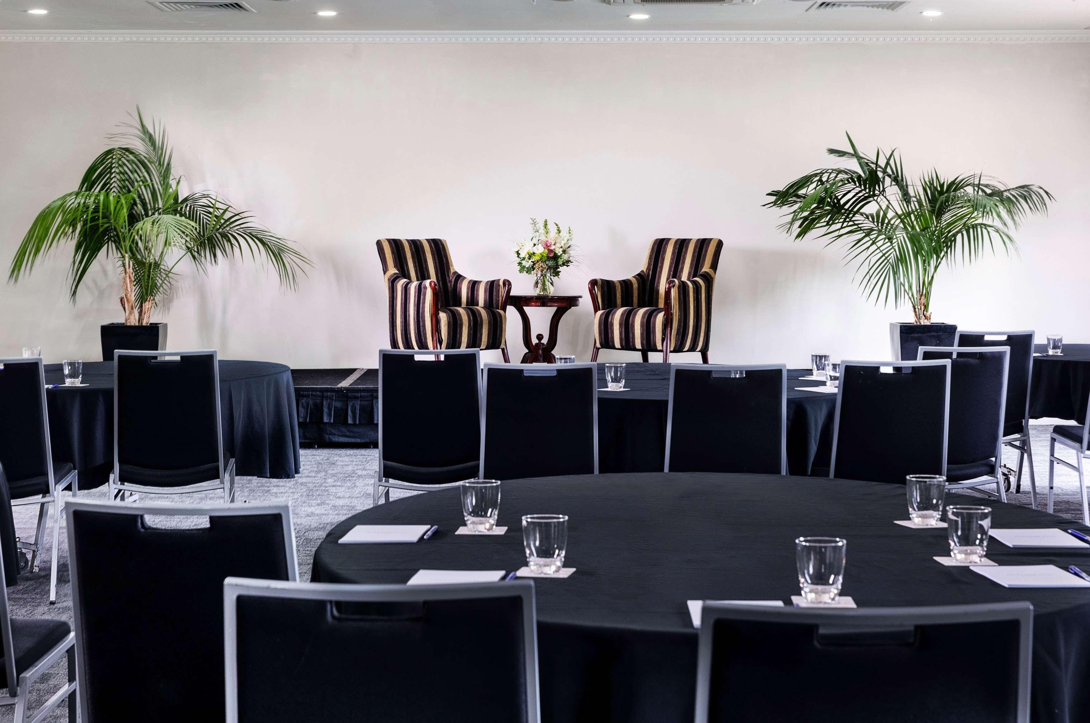 A conference room with a round table, black chairs, and potted plants.