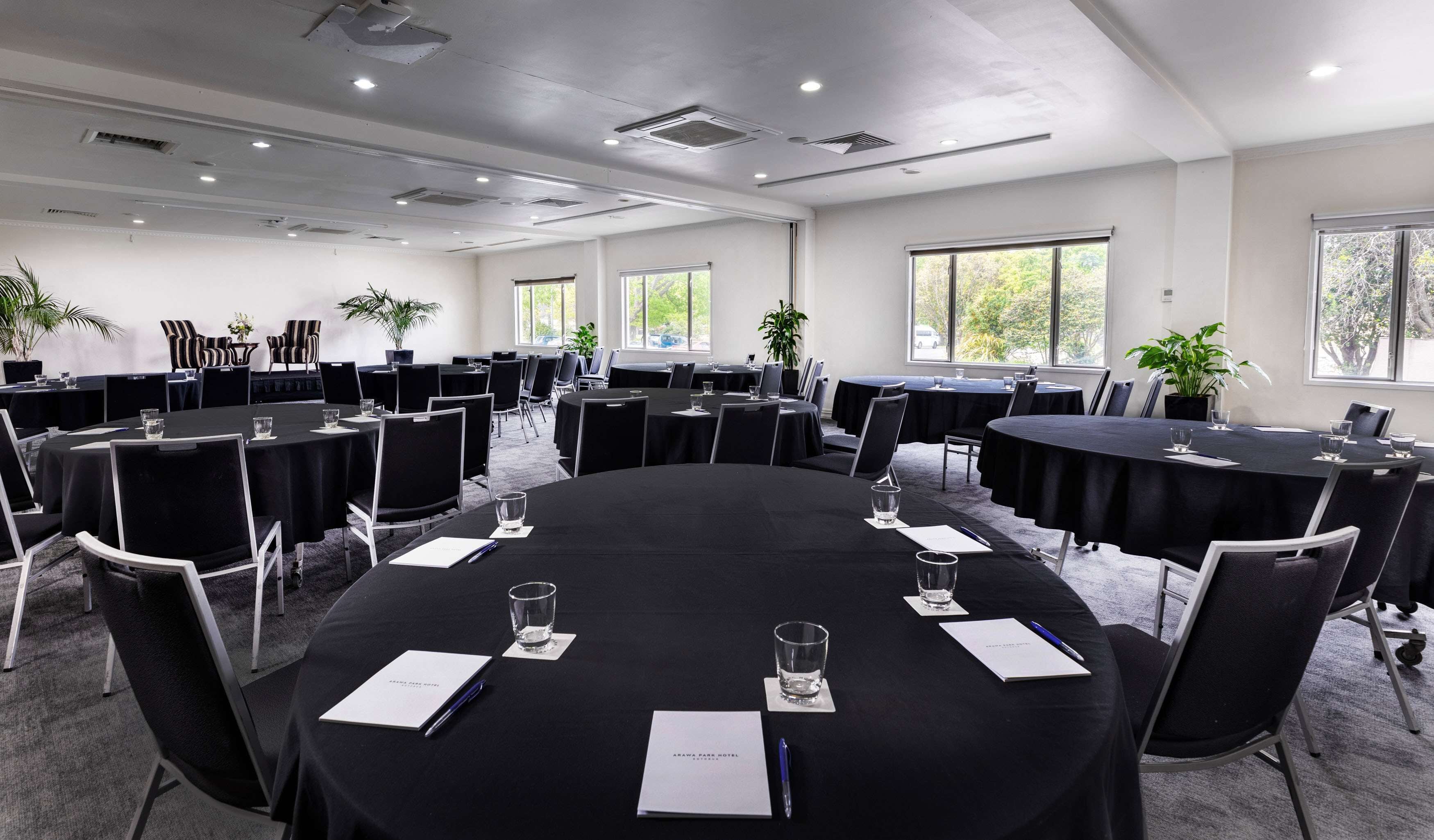 A conference room with multiple tables, chairs, and potted plants.