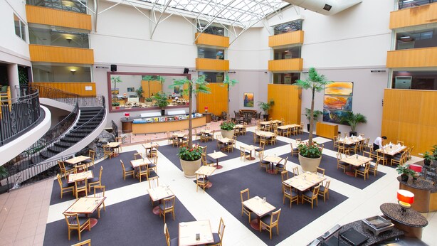 Un espacio interior amplio con varias mesas y sillas para comer, una barra central y una escalera.