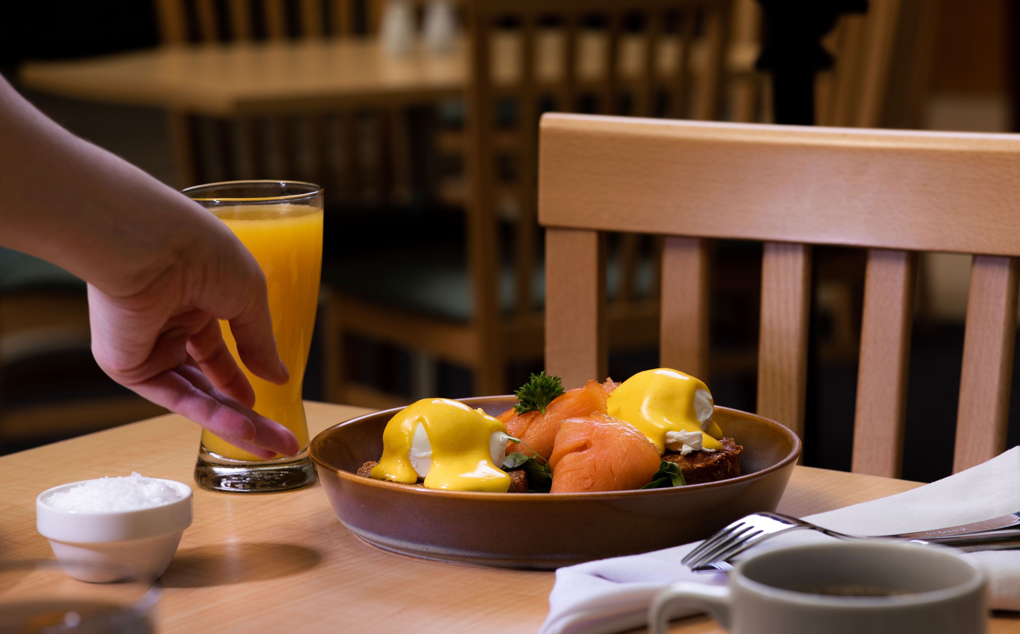 Une table mise pour le petit-déjeuner avec un bol de œufs Bénédicte, un verre de jus d’orange et un petit bol de sucre.