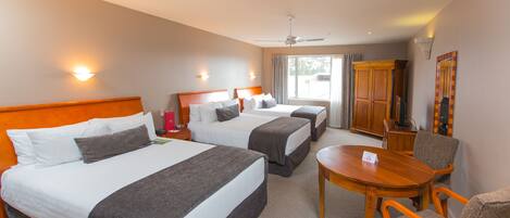 Een hotelkamer met drie bedden, een eettafel en een televisie.