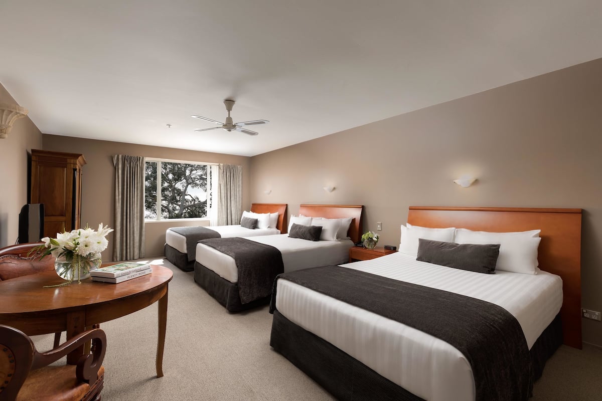 A hotel room with two beds, a wooden table with a vase of flowers, and a window with curtains.
