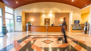 Un vestíbulo de hotel con una mesa de recepción, una planta grande en maceta y una exhibición de folletos.