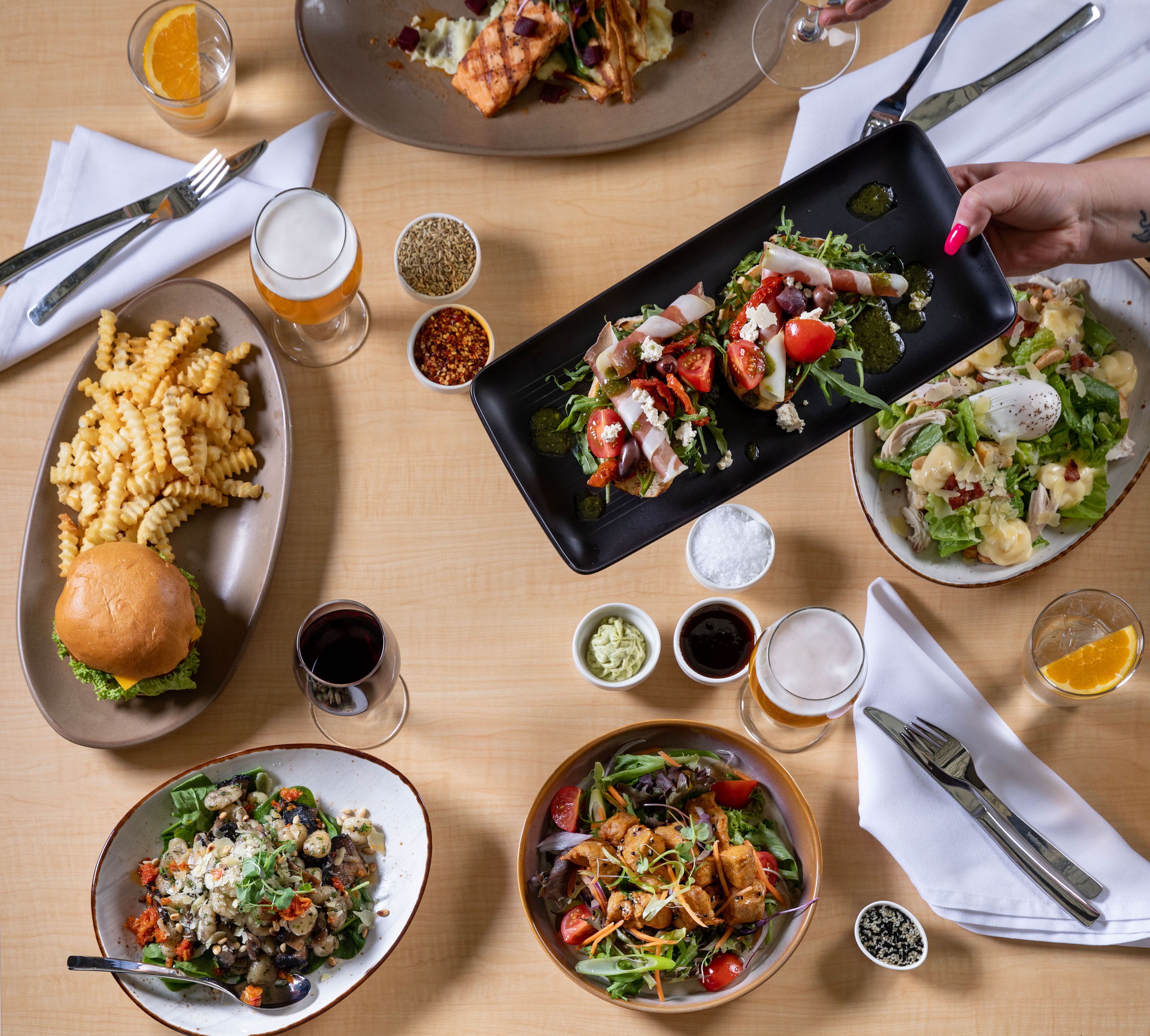 A dining table with various dishes, including pasta, salads, and a burger.