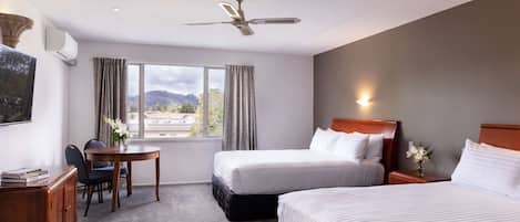 A hotel room with two beds, a desk, a chair, a ceiling fan, and a window with curtains.