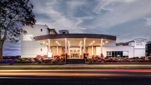 Un hotel moderno con un toldo de entrada circular, un letrero que indica 'Arawa Park Hotel' y un jardín bien cuidado.