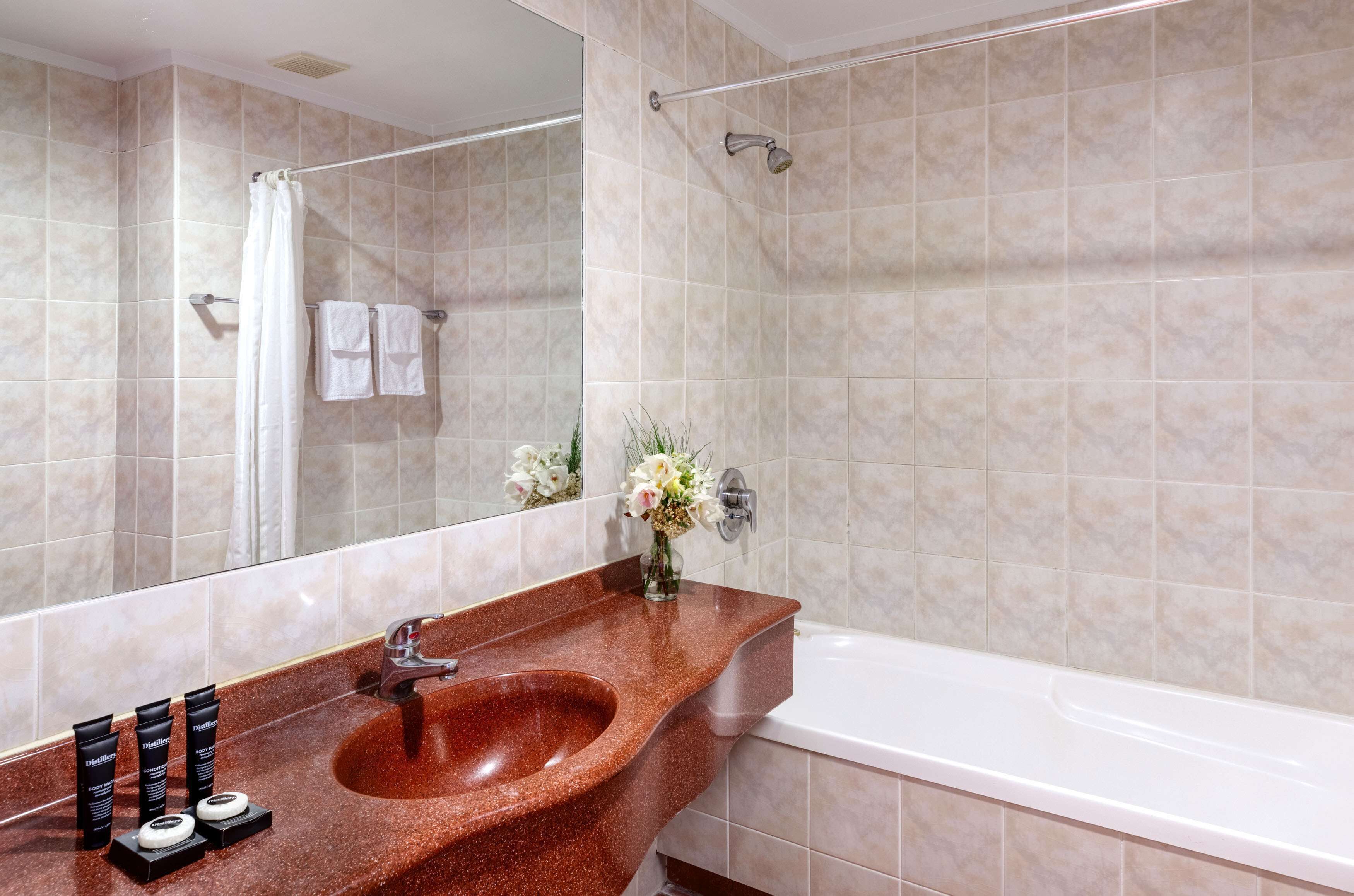 Une salle de bain avec un lavabo en granit, une baignoire blanche et des murs recouverts de carreaux beiges.